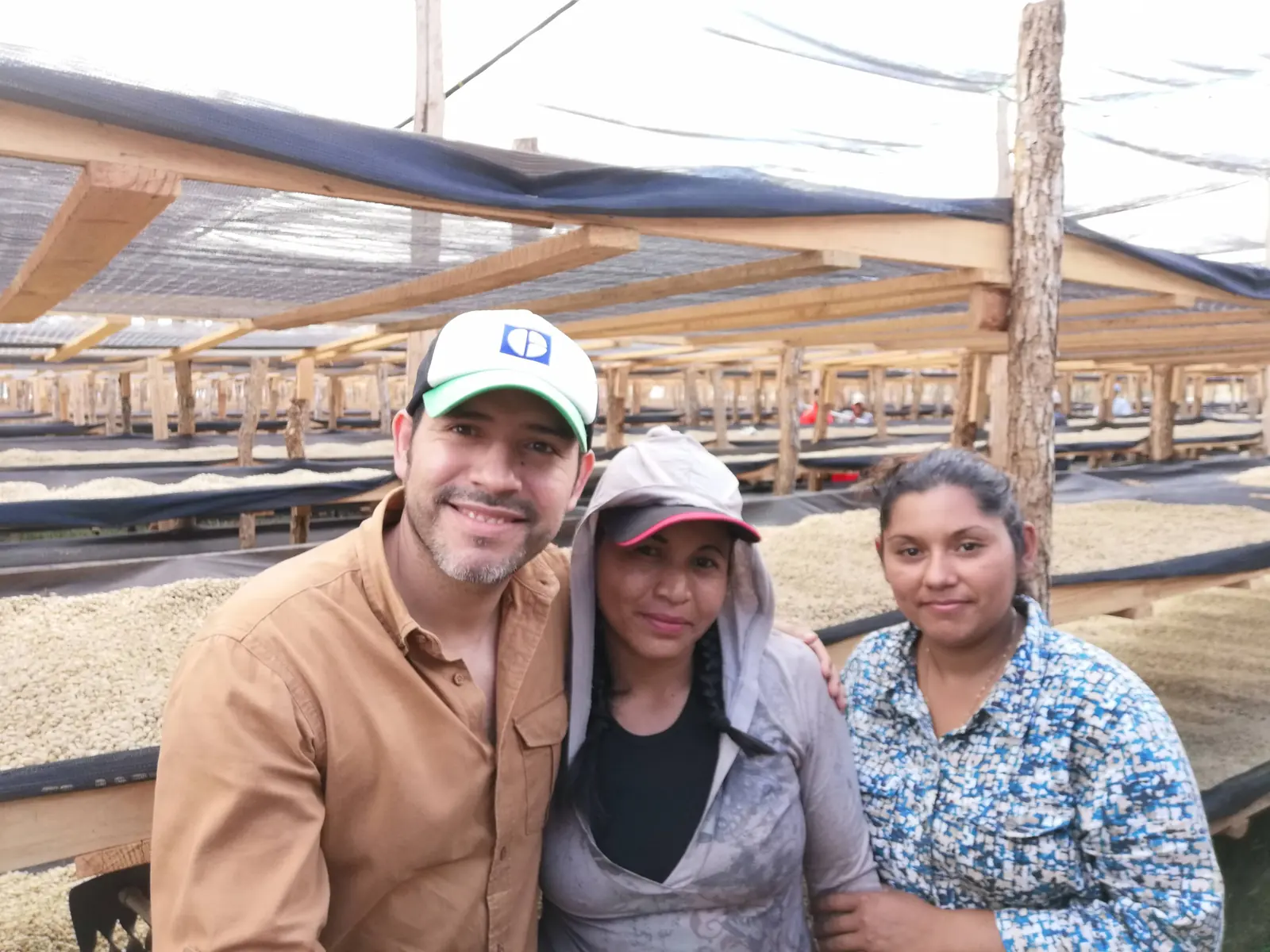 Miembro del equipo de Esperanza Harvest con dos productoras frente a camas africanas de secado